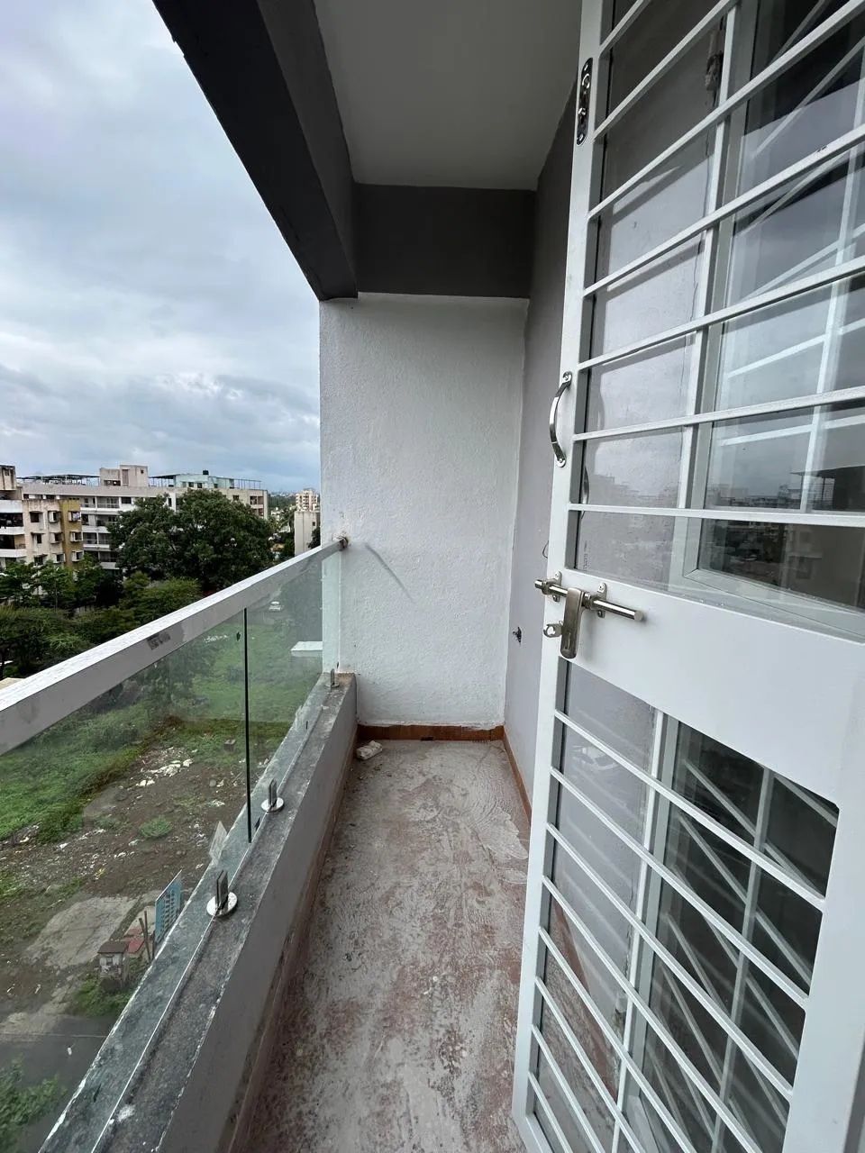 Balcony with glass railing overlooking Amrutdham greenery at Prabhupushpa Residency