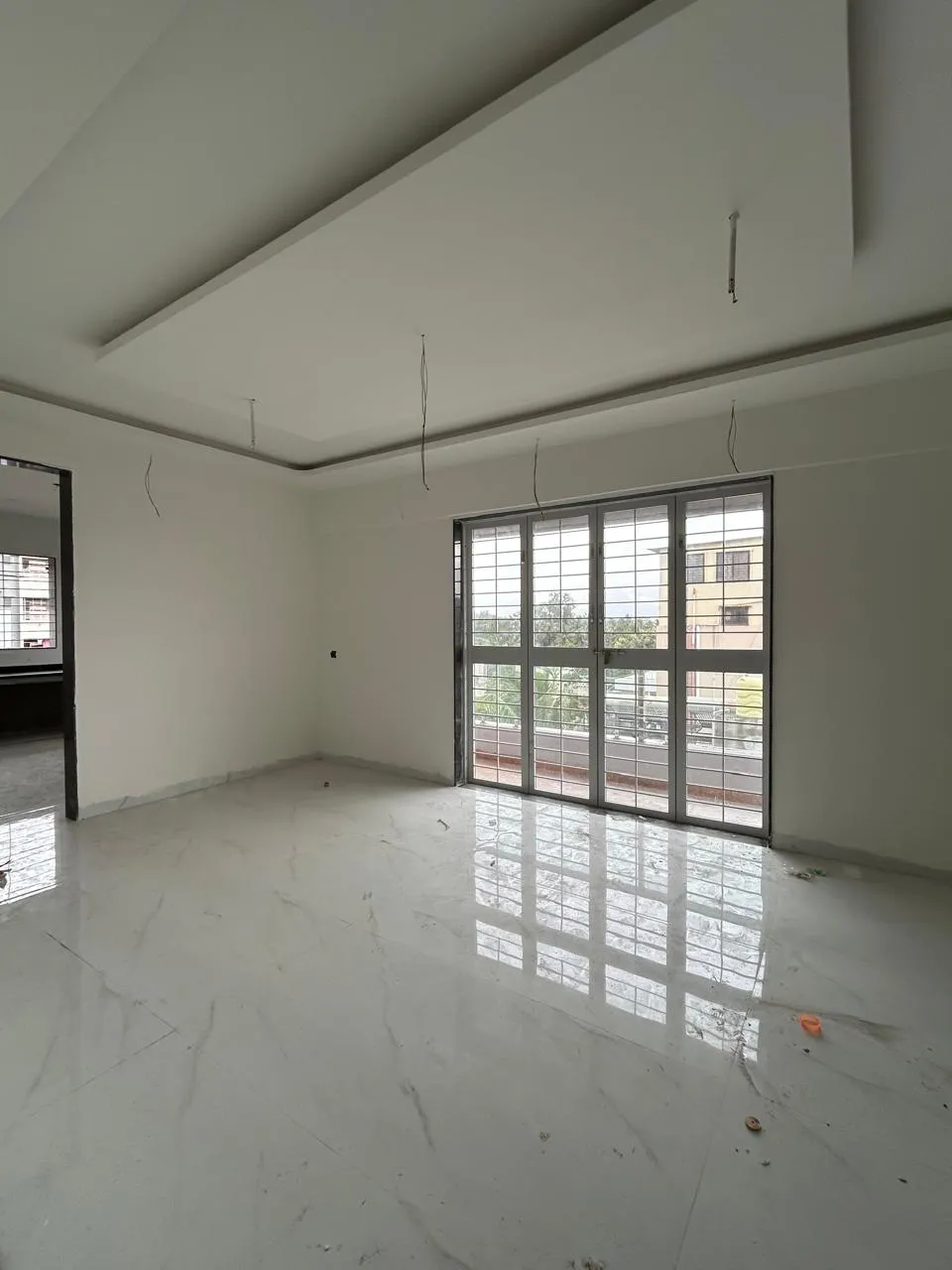 Spacious 3 BHK living room with false ceiling, vitrified flooring and French windows to the balcony